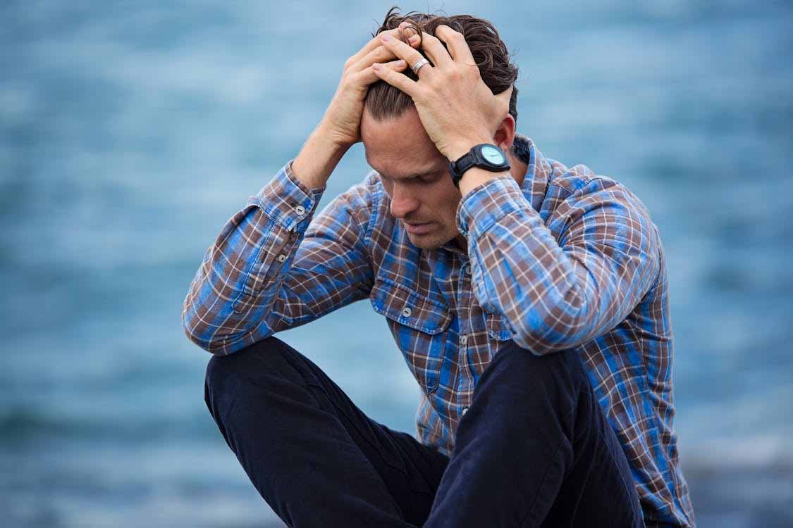 man-sitting-outdoors-holding-his-head-reflecting-emotional-stress-and-fatigue-linked-to-low-testosterone-symptoms